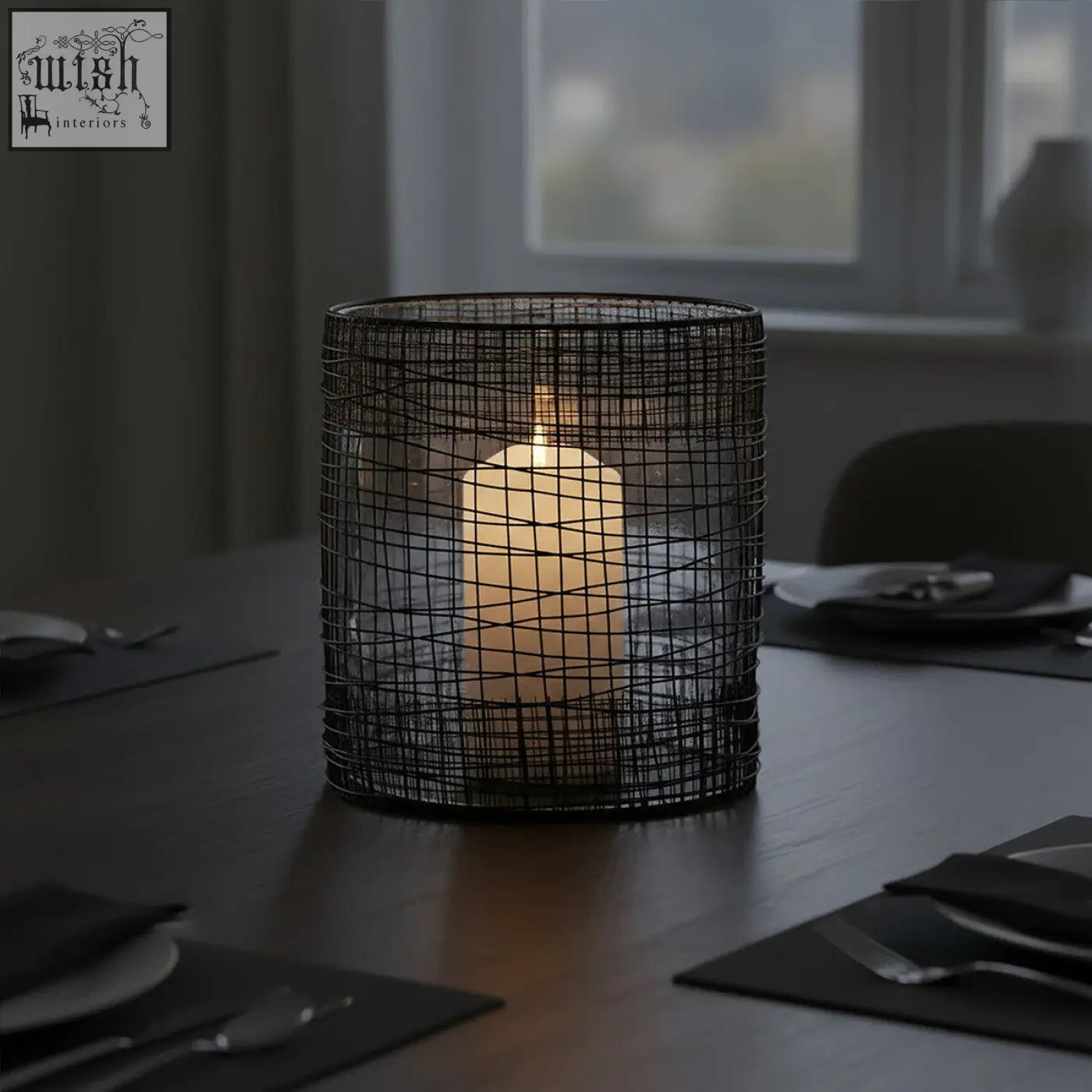 Black wire mesh trento cylindrical lantern with a lit white pillar candle inside for cozy lighting