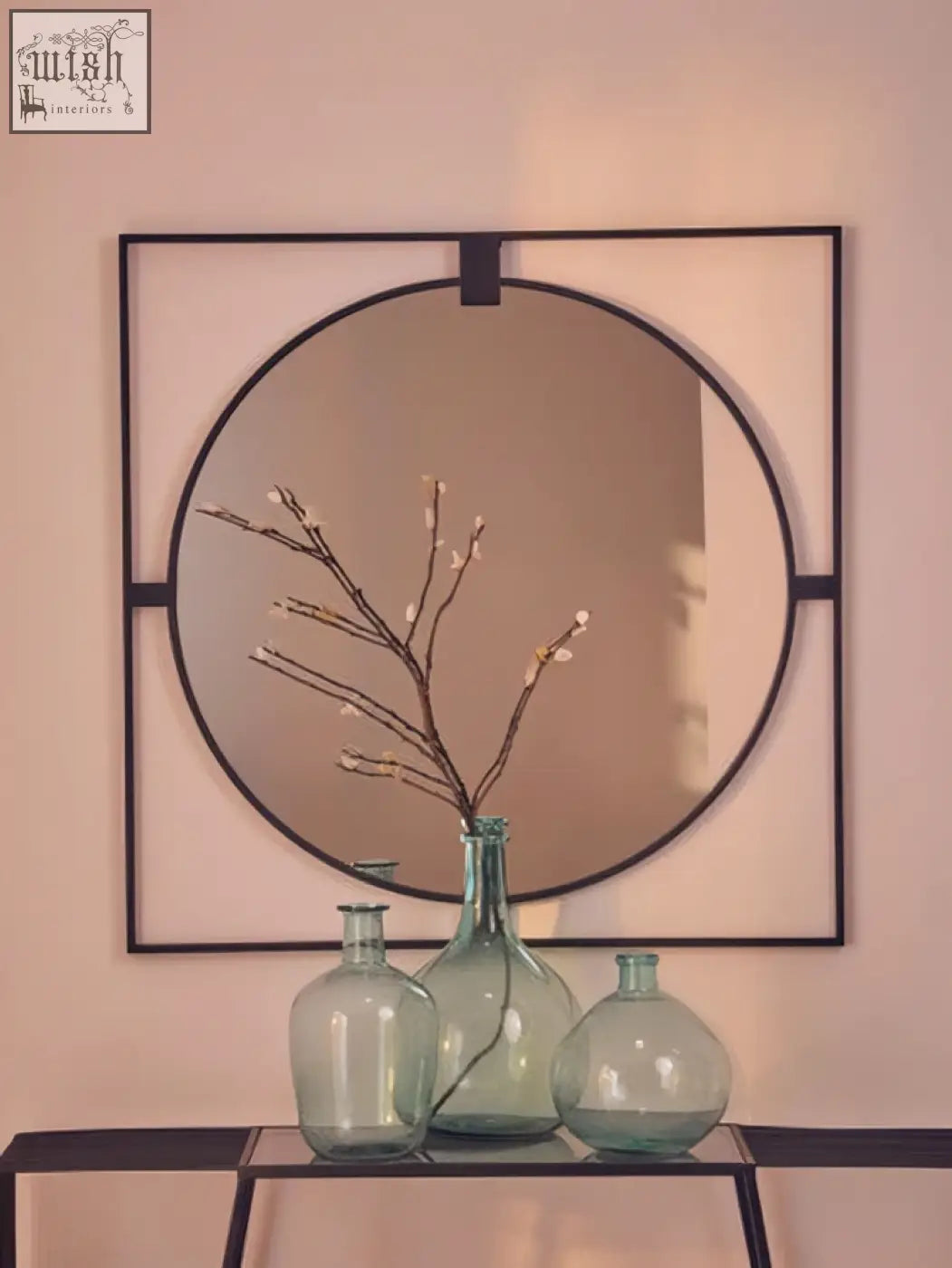 Large square black metal frame round insert wall mirror with frosted glass center above green glass vases