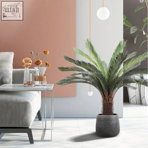 A lush green tropical artificial palm with plastic palm leaves in a dark gray ceramic pot for indoor decor