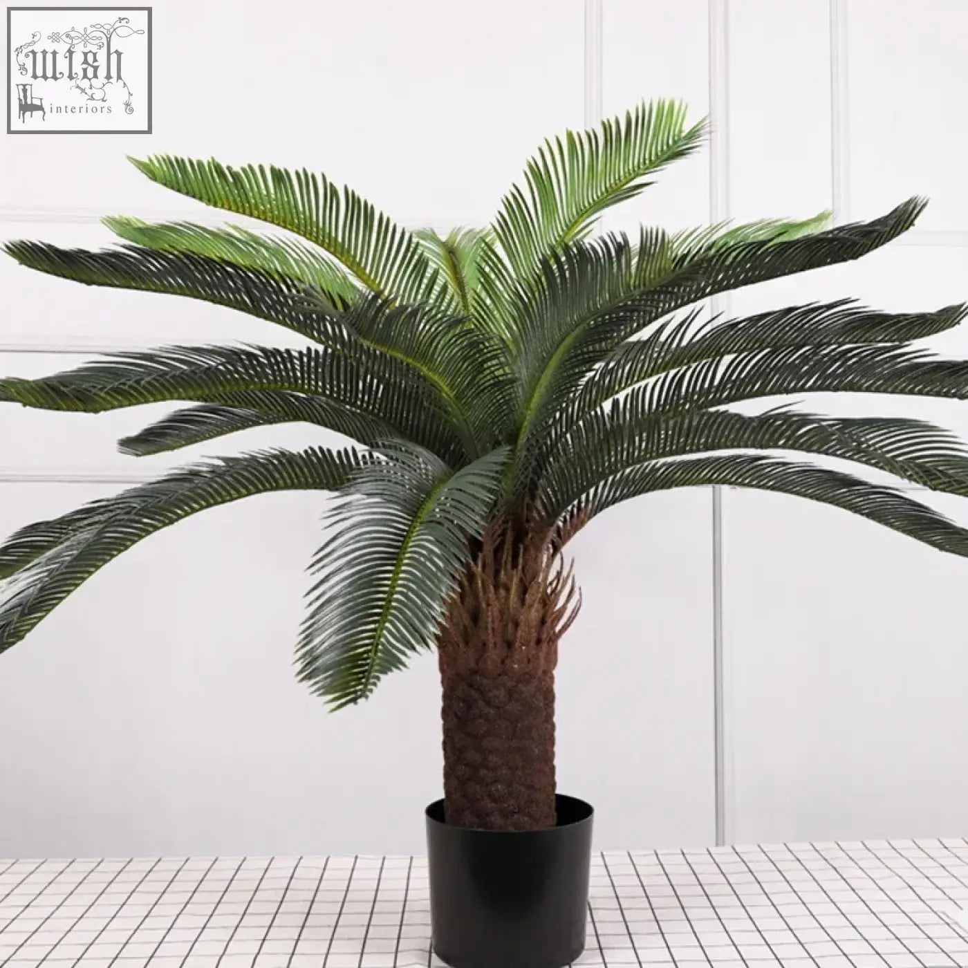 A tropical artificial palm tree with lush plastic palm leaves and a textured brown trunk in a black pot for decoration