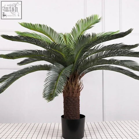 A tropical artificial palm tree with lush plastic palm leaves and a textured brown trunk in a black pot for decoration
