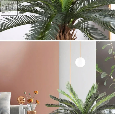 A sleek white pendant light with a thin gold chain hanging above a tropical artificial palm with plastic palm leaves
