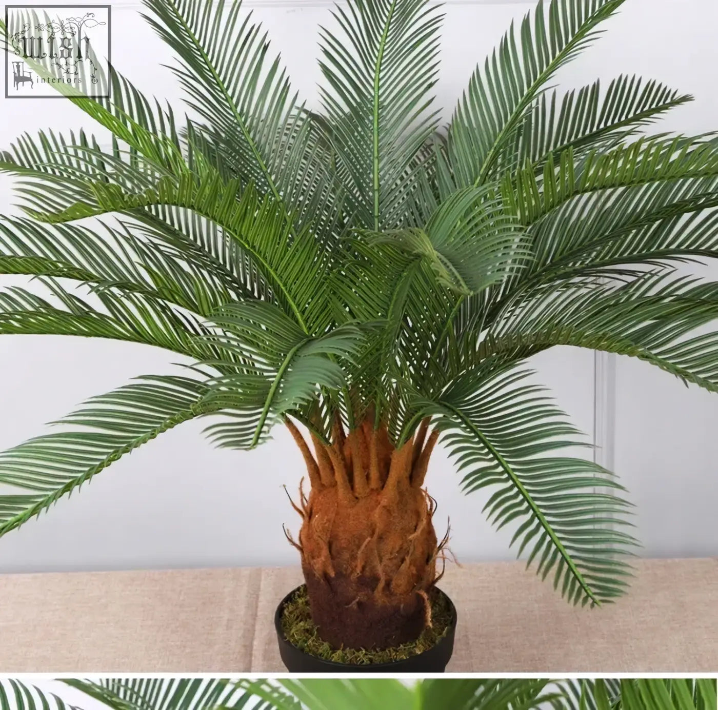 A tropical artificial palm tree with lush plastic palm leaves and textured brown trunk in a black pot for indoor decor