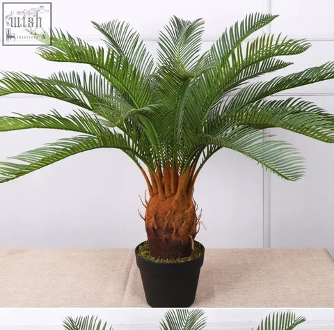 Green tropical artificial palm with plastic palm leaves and textured brown trunk in black pot for home or office decor
