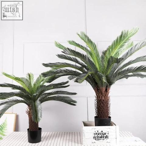 Two artificial cycad plants with dark green plastic palm leaves and brown textured trunks for tropical artificial palm decor