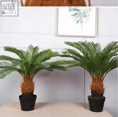 Two artificial palm trees with green plastic palm leaves and brown trunks in black pots for tropical decor