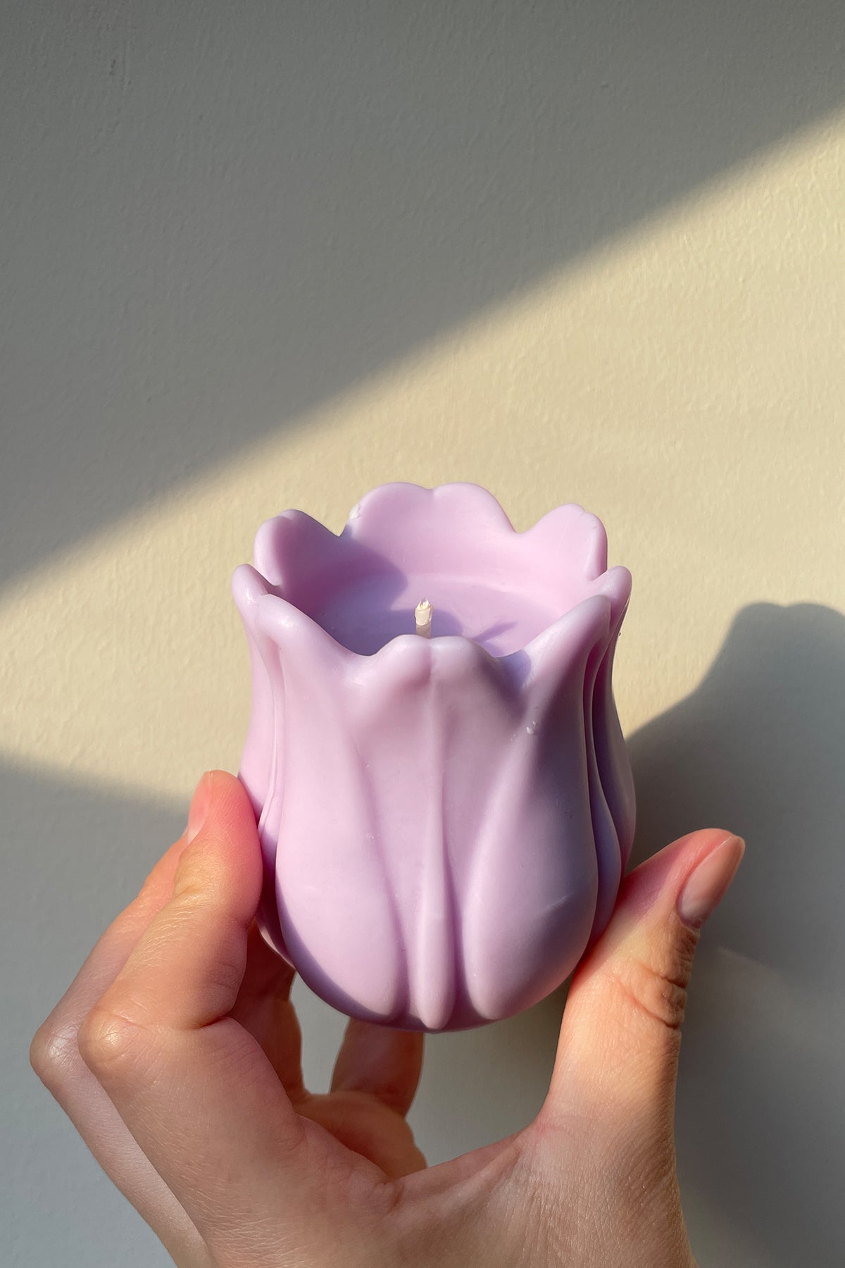 A delicate lavender tulip shaped candle with a smooth glossy finish and a single wick at its center