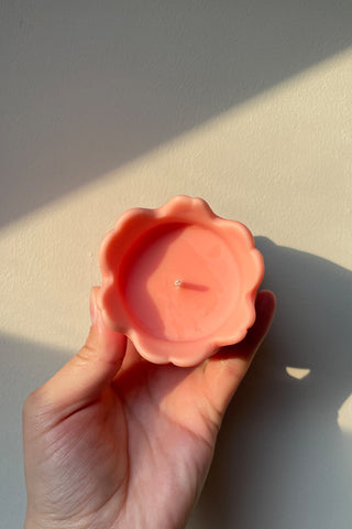 A peach-colored tulip shaped candle with a smooth glossy finish and single wick at its center