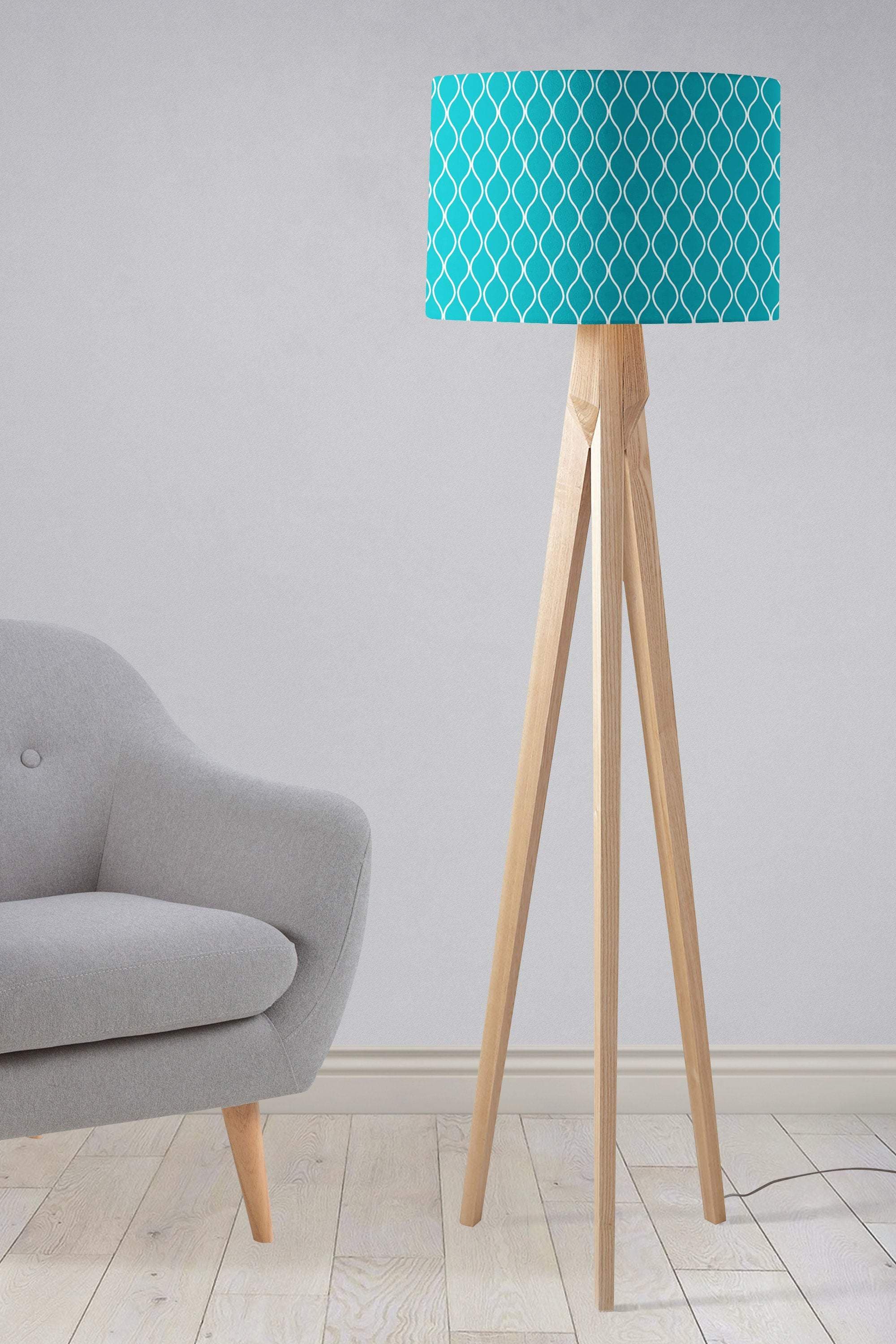 Teal table lamp with a white geometric design fabric lampshade on a light wood tripod base
