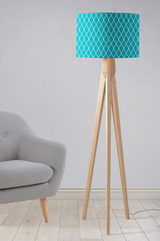 Teal table lamp with a white geometric design lampshade on a light wood tripod base