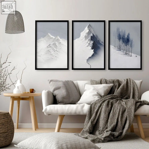 Three framed black and white mountain landscape wall art prints in grey white and blue hang above a sofa in a living room