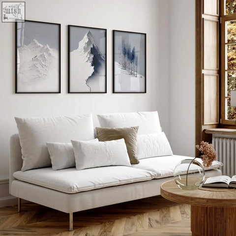 White upholstered sofa with metallic legs and cushions in living room featuring scandi nordic mountain landscape wall art