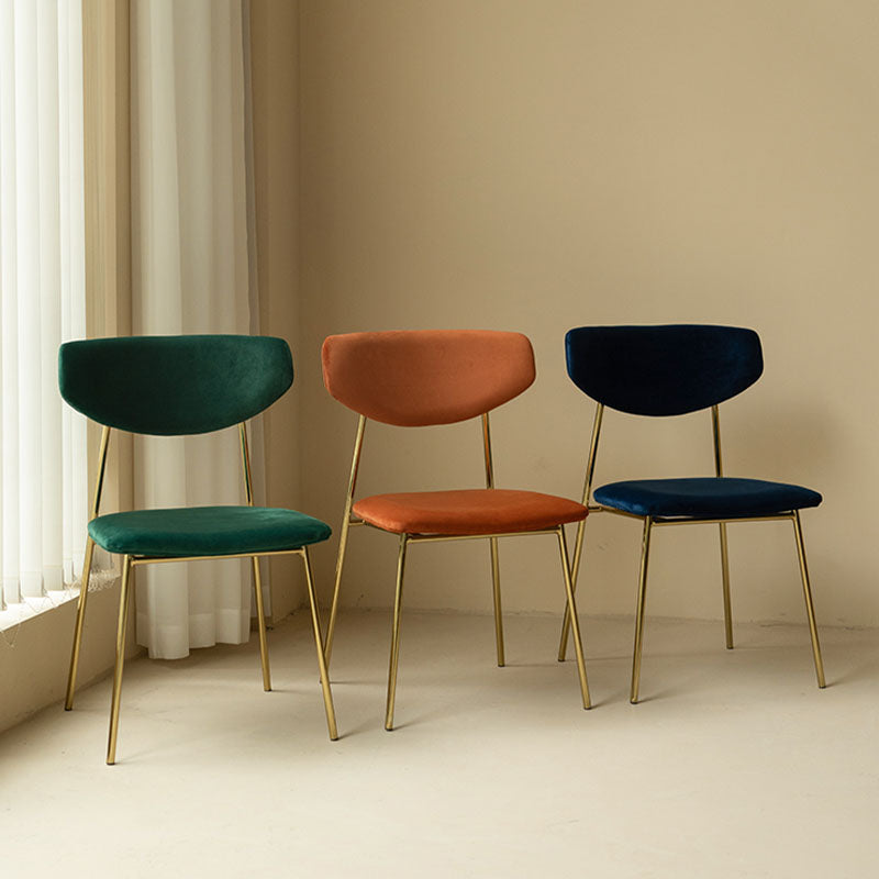 Three modern urban dining chairs with velvet upholstery in emerald green terracotta and navy blue with gold frames