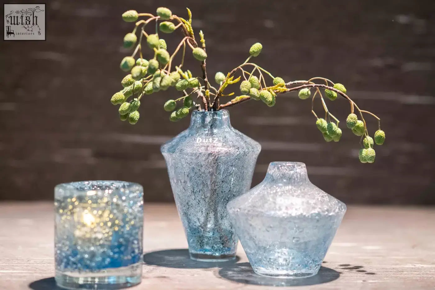 A blue bubbles vase and diffuser from dutz collection made of mouth blown glass with textured crackled surface holding green berries