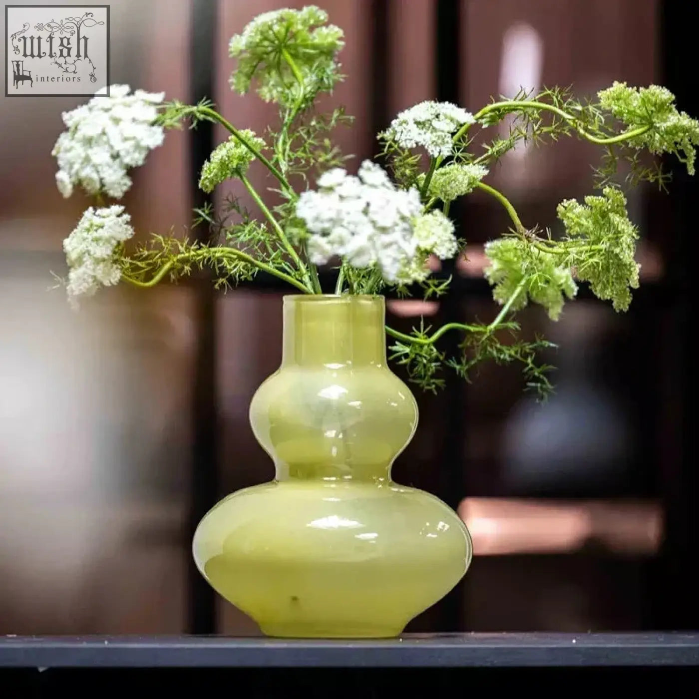 A mouth blown glass vase eldorado in chartreuse green with a double gourd shape holds white and green flowers