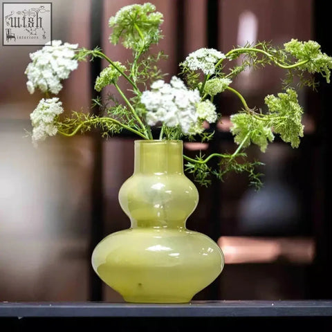 A mouth blown glass vase eldorado in chartreuse green with a double gourd shape holds white and green flowers