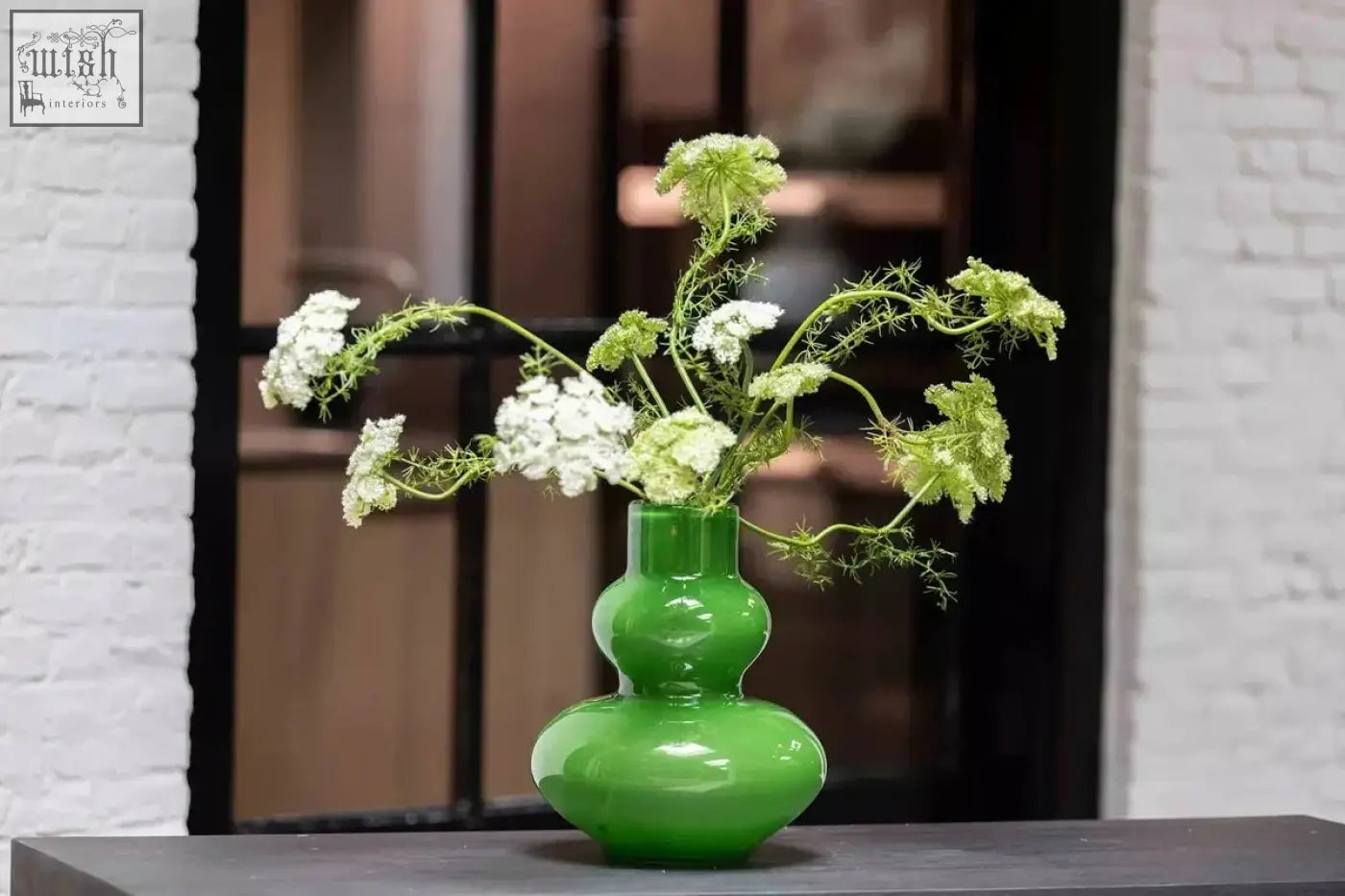 Glossy emerald green mouth blown glass vase eldorado from dutz collection holding white pale green wildflowers