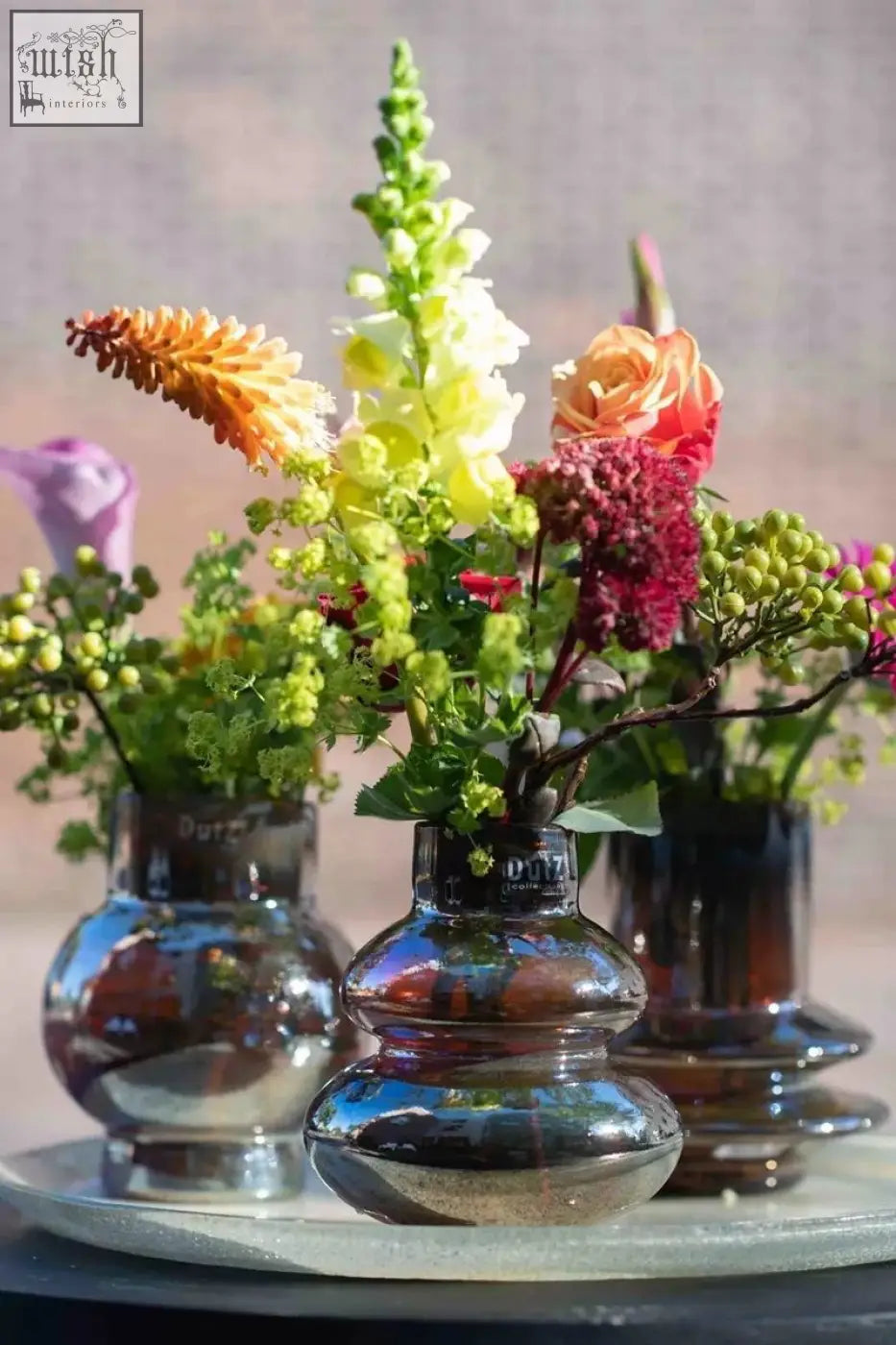 A trio of mouth blown glass vases from dutz collection in gold luster holding colorful snapdragons and roses