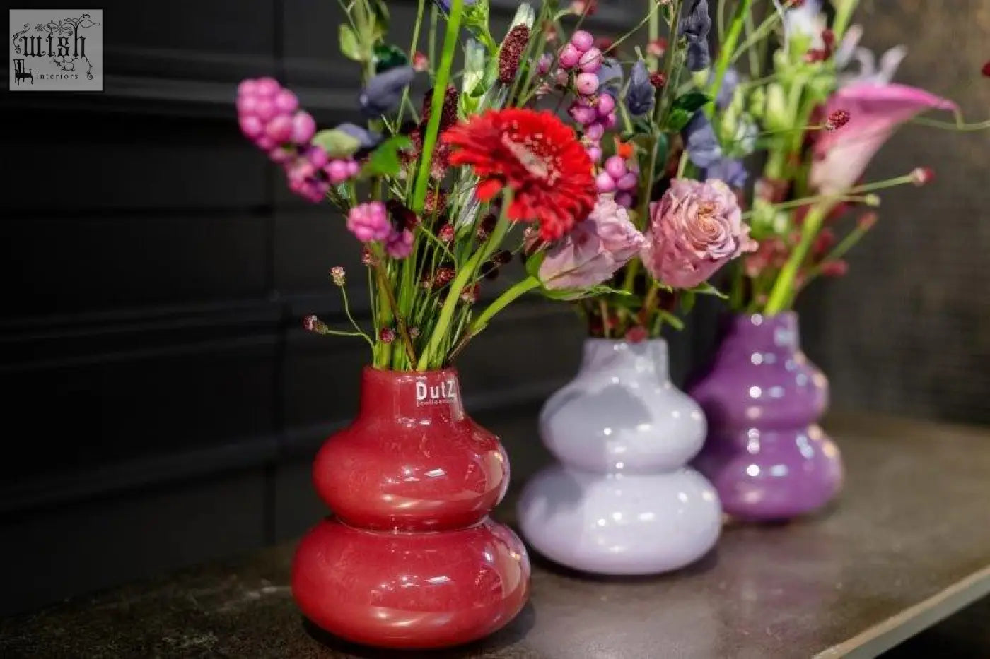 Three stacked glossy mouth blown glass vases in red lavender and purple from dutz collection holding fresh flowers