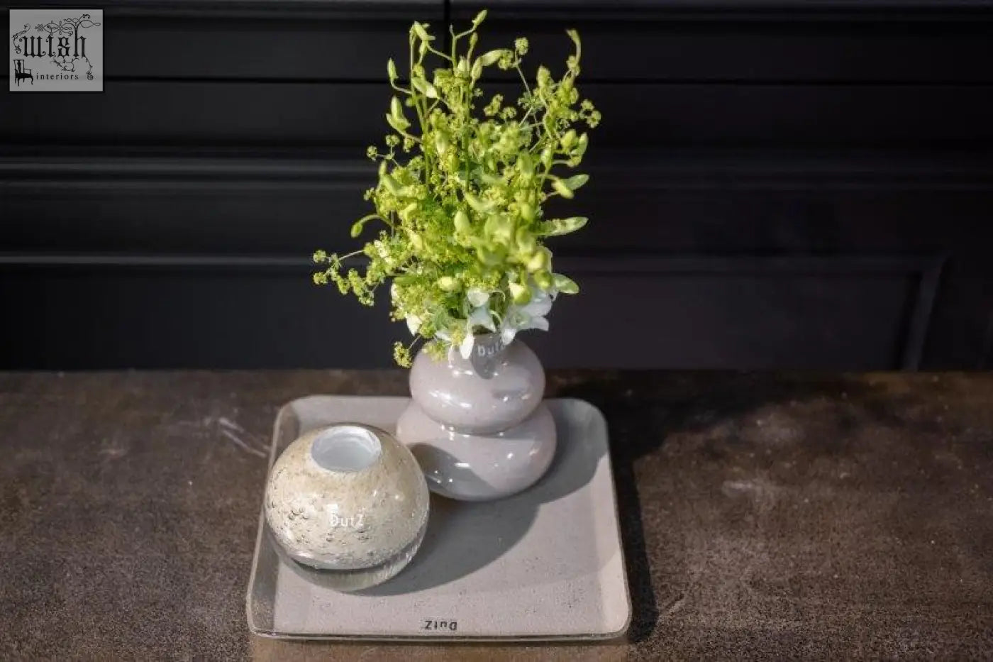 A sleek two-tiered gray ceramic vase from the dutz collection holds delicate green and white flowers in jungle green