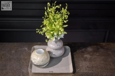 A sleek two-tiered gray ceramic vase from the dutz collection holds delicate green and white flowers in jungle green