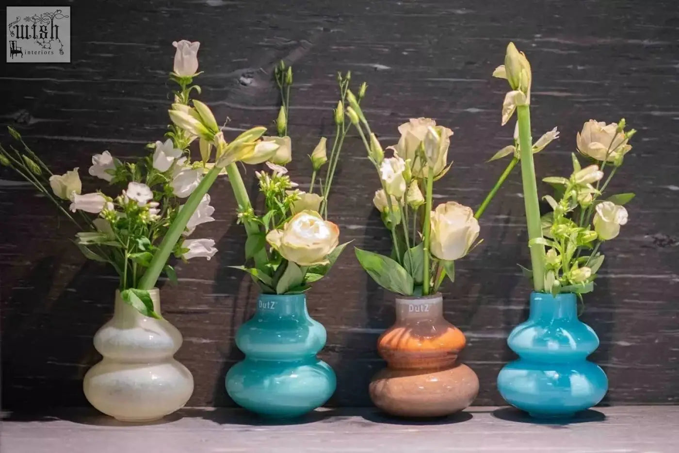 Four stacked gourd-shaped mouth blown glass vases in white teal terracotta and blue from dutz collection holding cream flowers