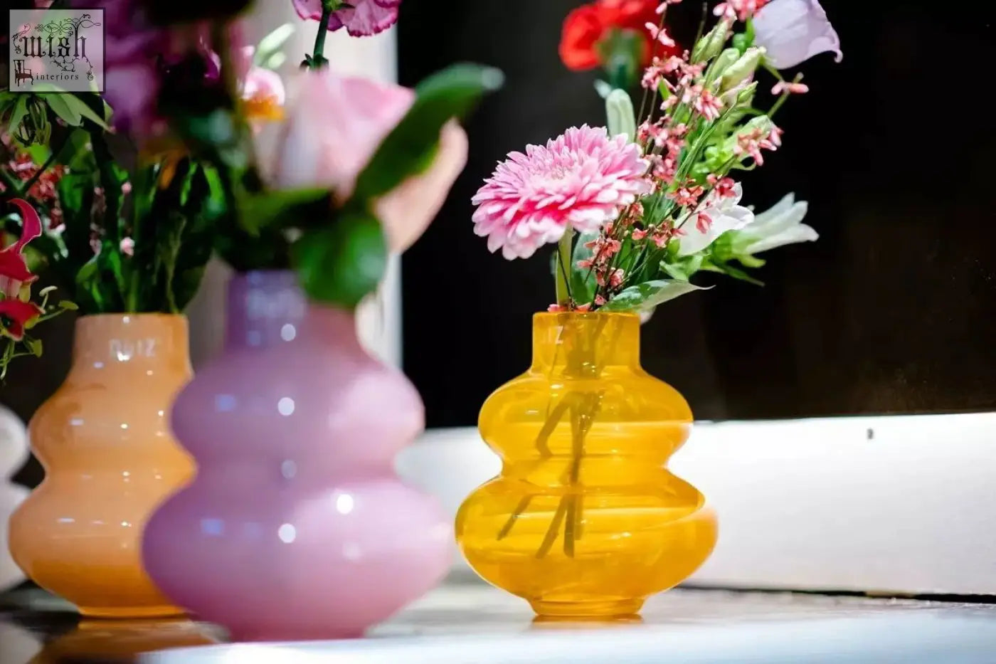 A mouth blown translucent yellow glass vase from dutz collection with an hourglass shape holding pink and white flowers