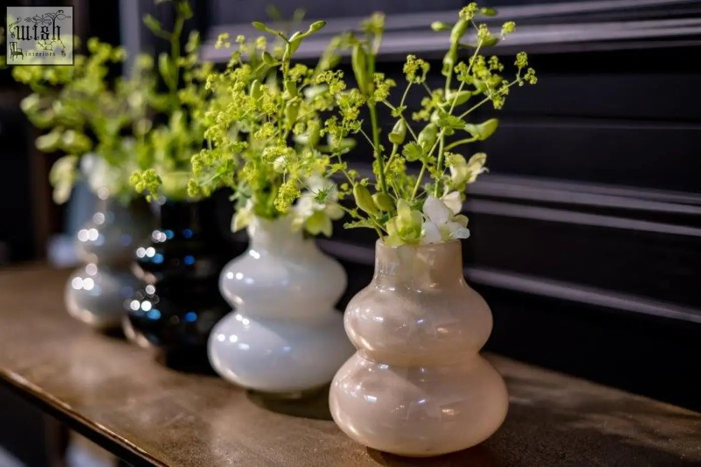 A mouth blown translucent peach-colored double gourd vase from dutz collection holding greenery and white flowers