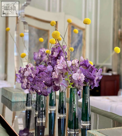 Elegant purple orchids in vibrant yellow blooms arranged in mouth blown dark green glass vase from dutz collection