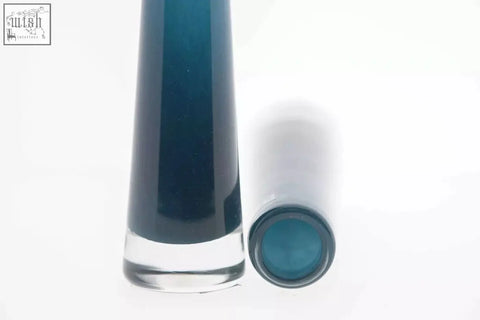 A sleek transparent glass vase solifleur from dutz collection with mouth blown dark teal liquid and matching teal cap