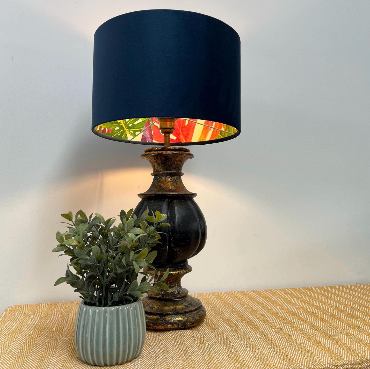 Dark blue velvet double sided drum lampshade with vibrant tropical leaf pattern inside on ornate brass base ceiling light shade