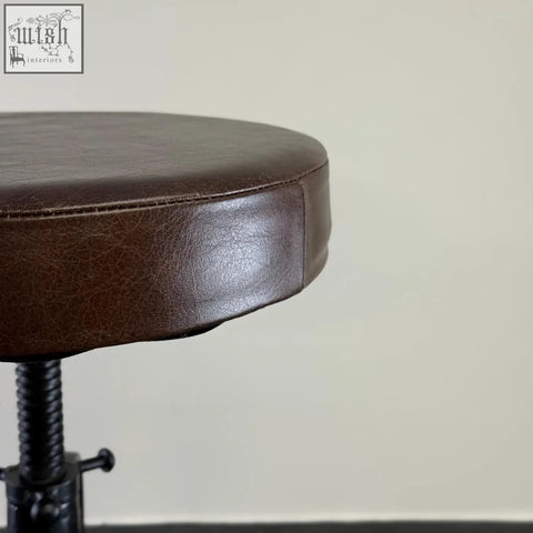 Brown faux leather bar stool with rounded seat and black cast iron adjustable height base for industrial use