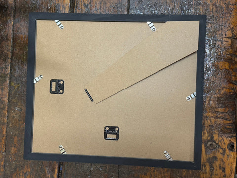 Back of a black rectangular picture frame with cardboard backing and metal hanging hardware for Victorian anatomy engraving