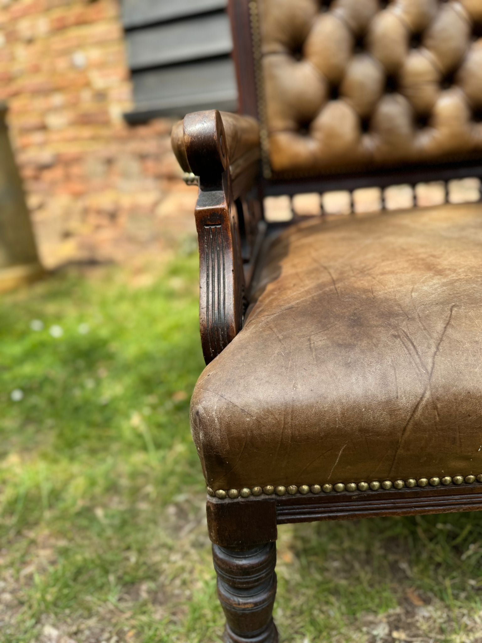 Victorian carved walnut library chair with tufted brown leather and brass nailhead trim for fireside comfort