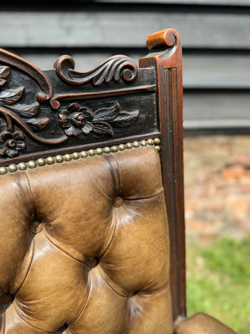 Victorian carved walnut library chair with dark brown floral details and a tufted tan leather seat for fireside use
