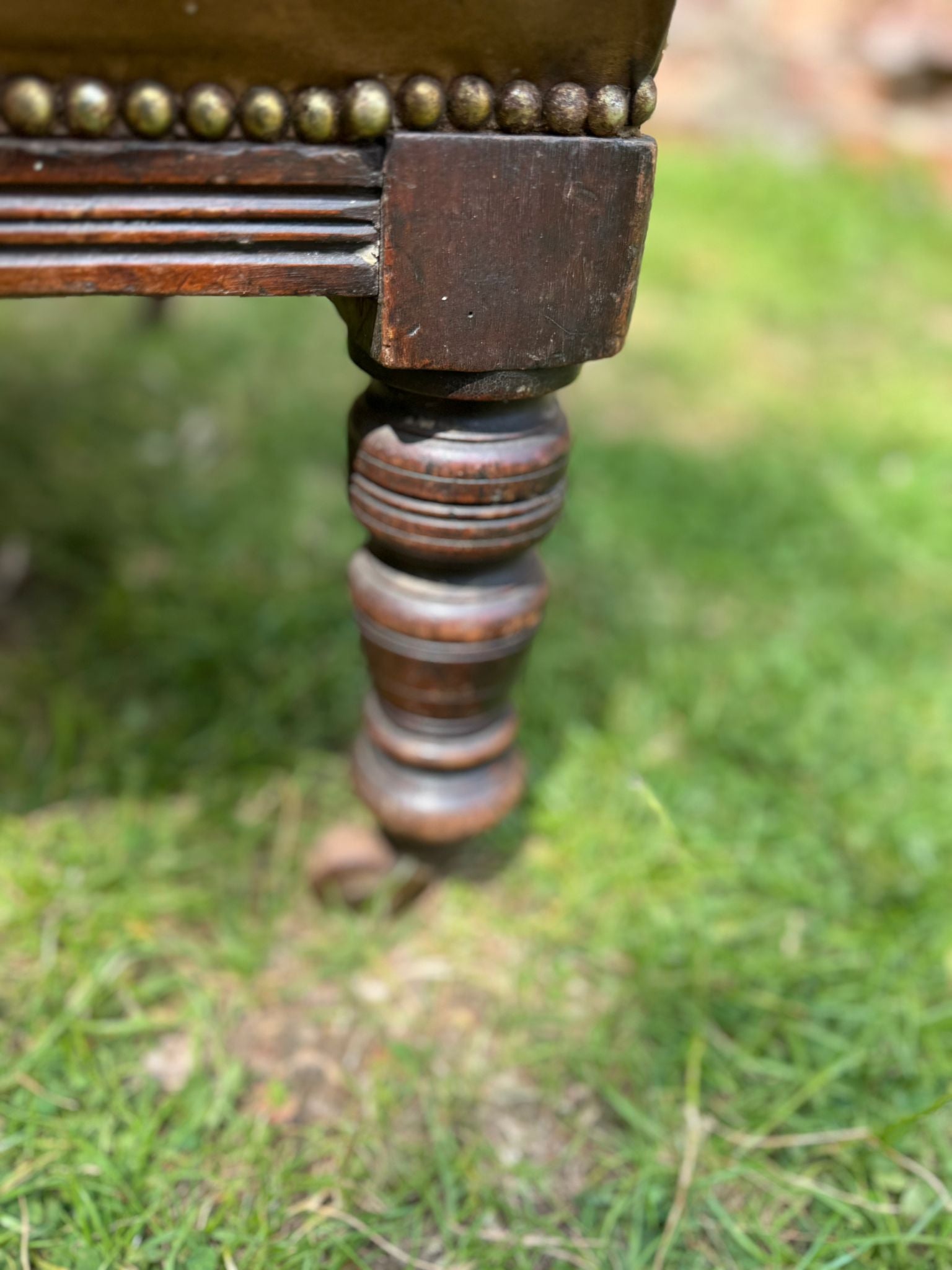 Dark wood turned leg with decorative grooves and brass beaded trim on a carved walnut victorian fireside armchair