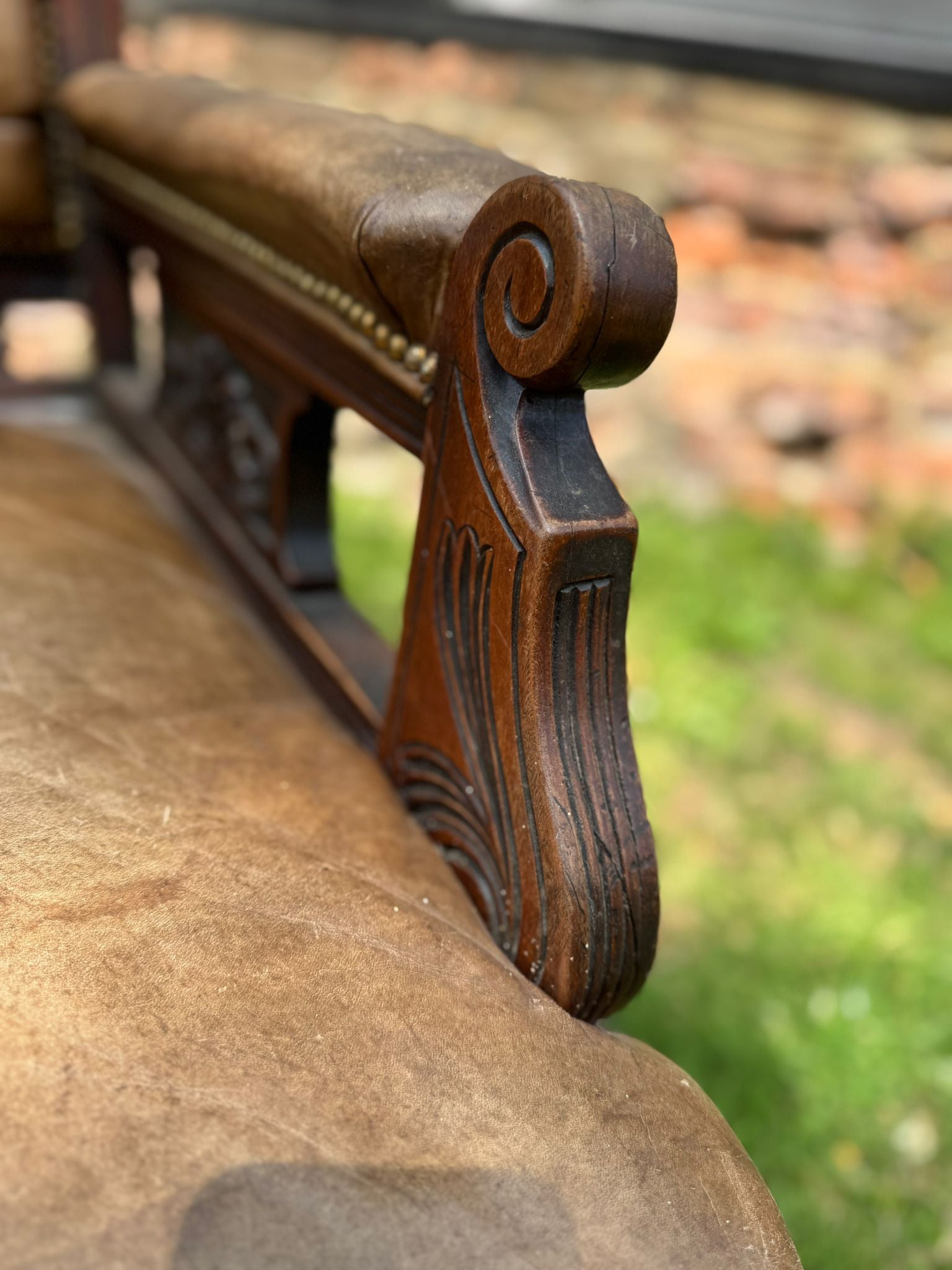 Antique carved walnut armrest with scrollwork and tufted brown leather seat on victorian library fireside chair