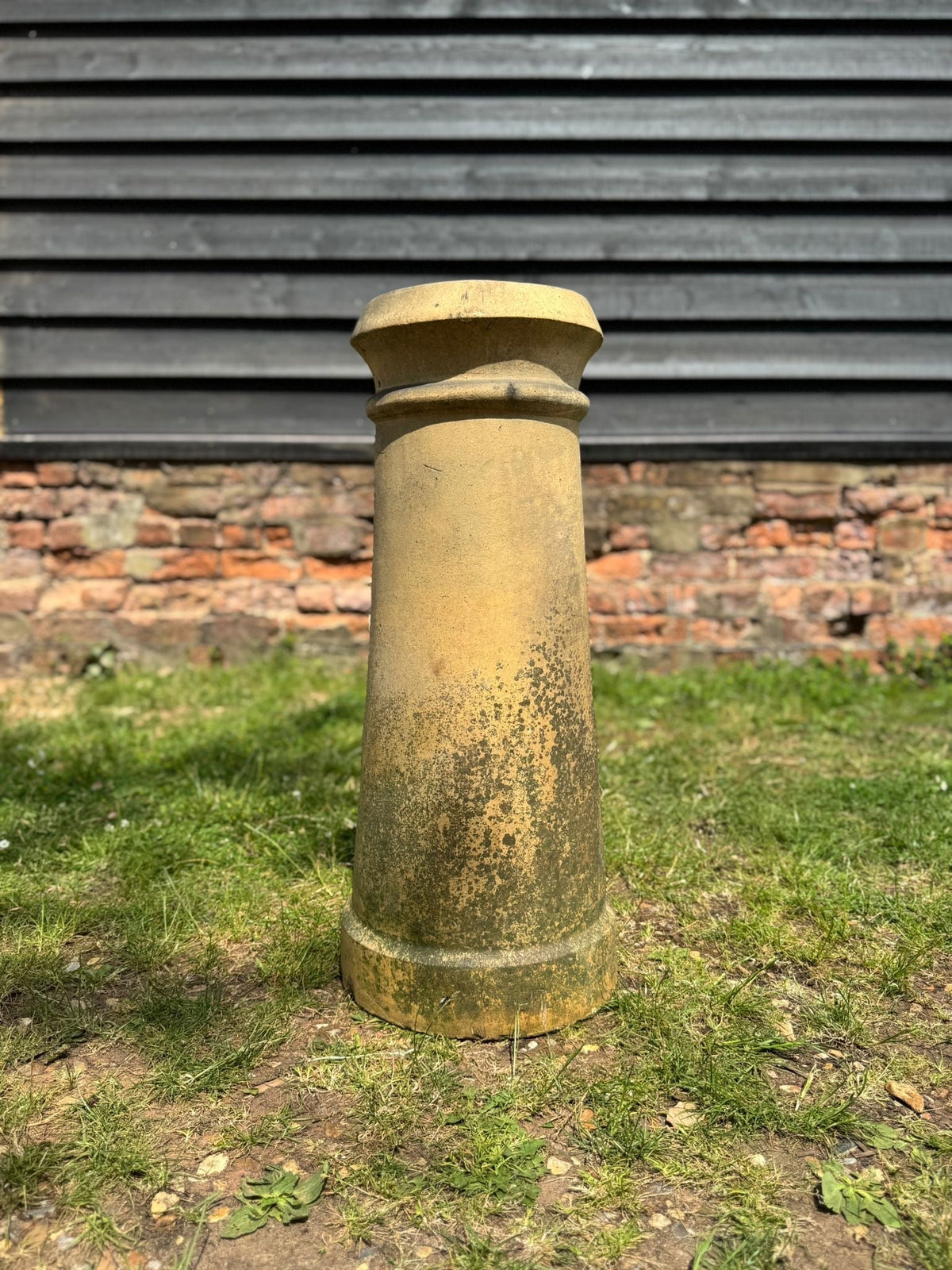 A weathered yellow terracotta chimney pot with a rolled rim and fluted top perfect as a garden planter