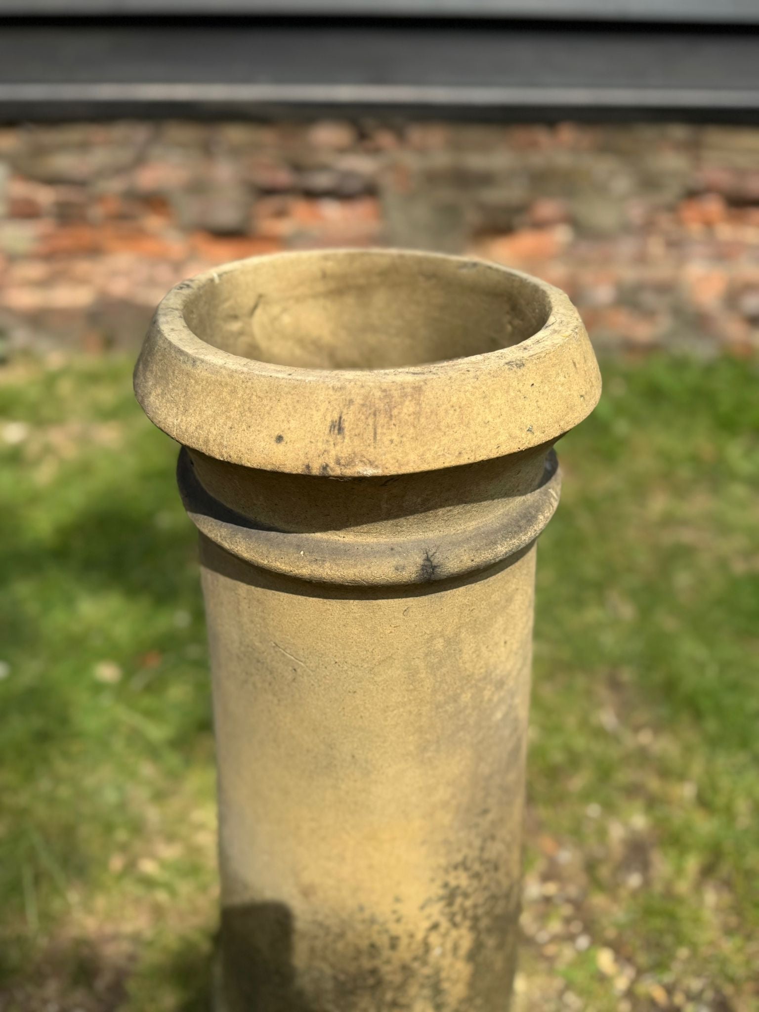 Weathered yellow terracotta chimney pot with rolled rim and flared top showing visible wear for garden planter