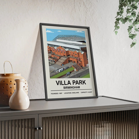 A framed villa park stadium print with a stylized illustration of red brick buildings and a modern roof against blue sky