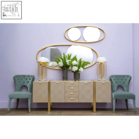 Beige console table with gold legs and drawers flanked by two teal blue velvet tufted dining chairs