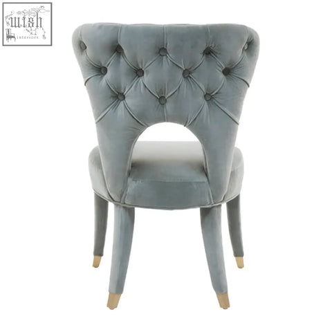 A tufted gray velvet dining chair with a curved back and gold-tipped legs perfect as a velvet tufted dining seat