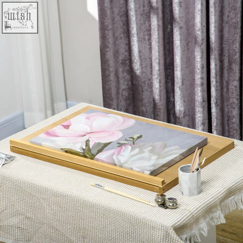Framed canvas painting of pink and white magnolia flowers on a light gray background in a portable folding beechwood table easel with adjustable angle