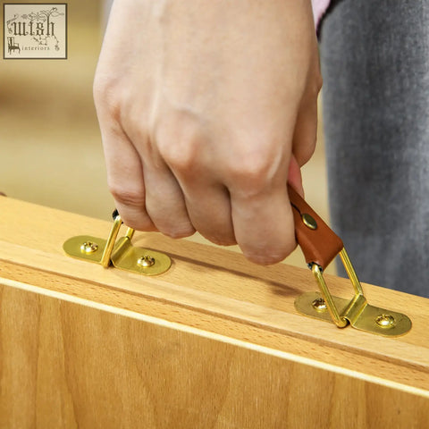 A hand gripping the brown leather handle and brass hardware of the vinsetto adjustable angle table easel box on light wood