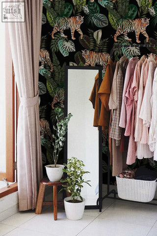 Black-framed full-length mirror beside rack of clothes and plants on vintage botanical wallpaper peel and stick mural