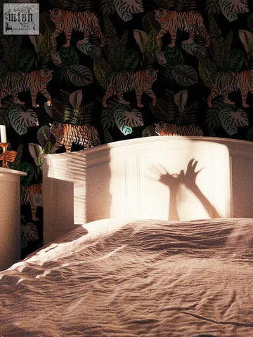 A white wooden headboard casting hand shadows on vintage botanical wallpaper with dark tropical plants and leopard print