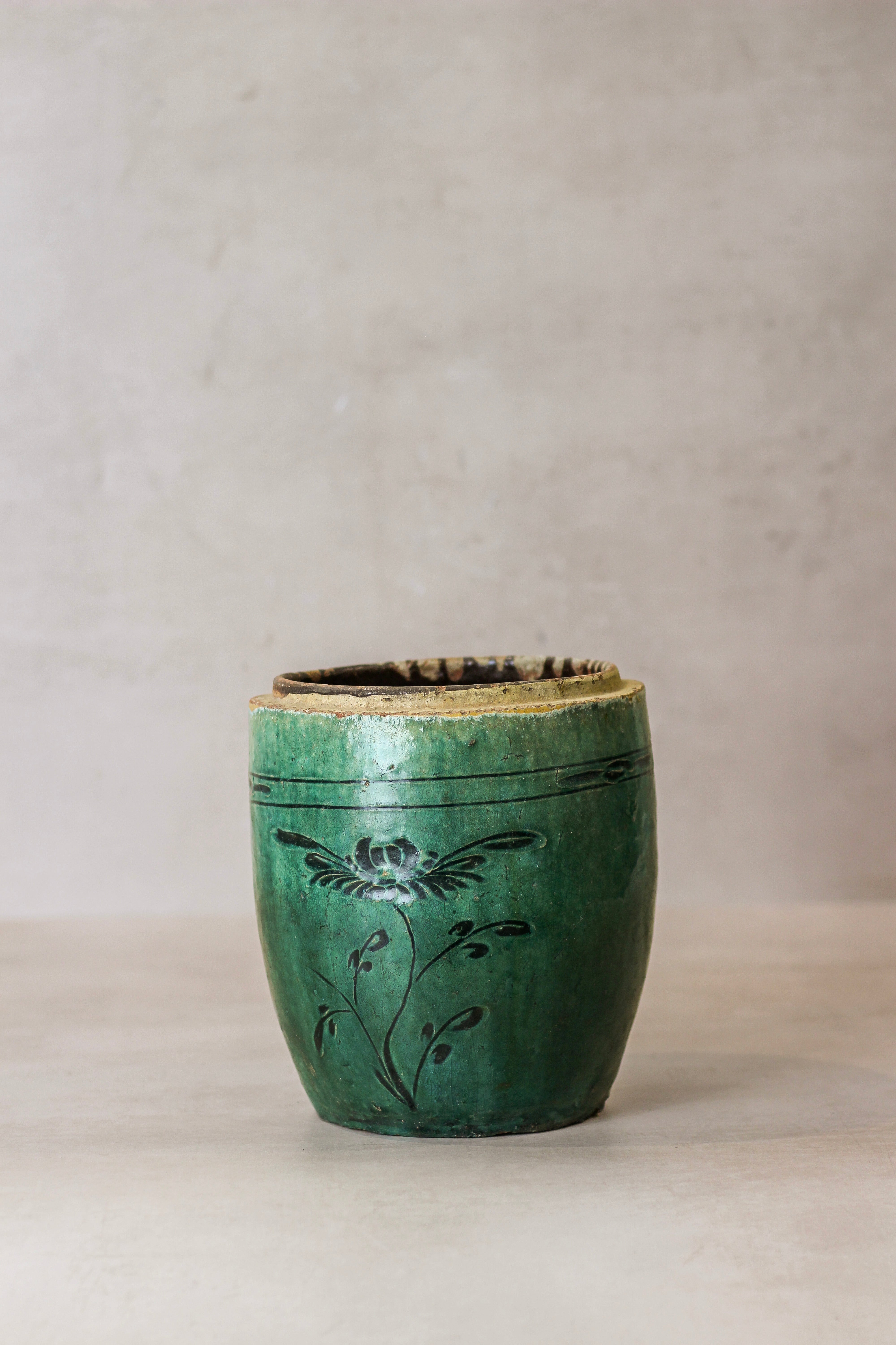 A vintage emerald green ceramic pot with black floral decals and a slightly chipped rim perfect for decor
