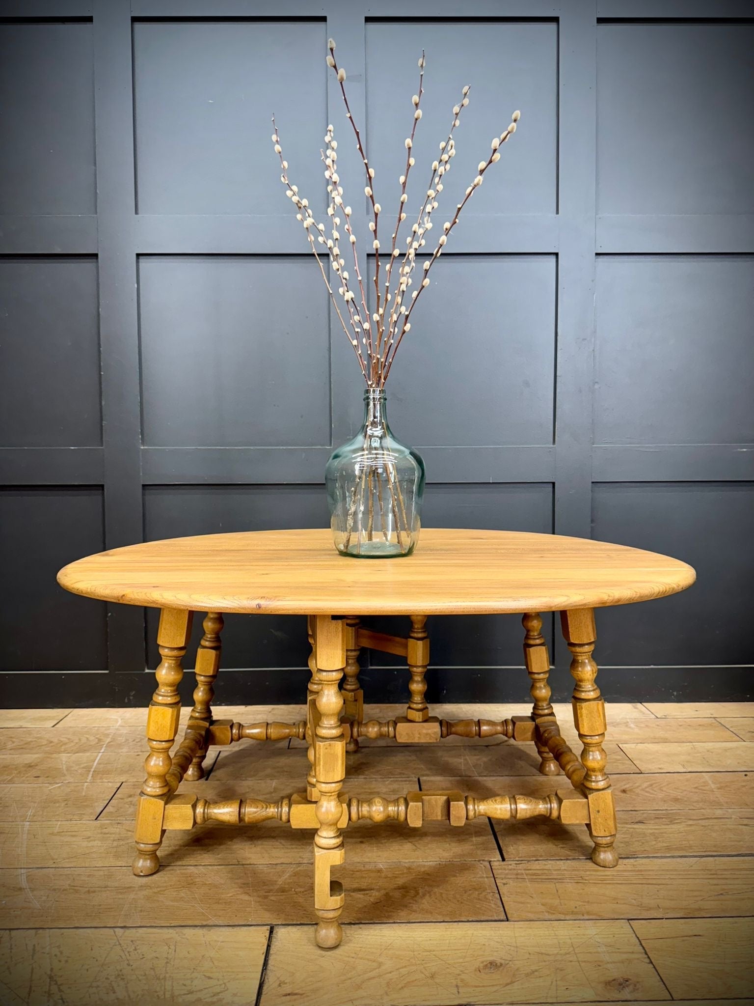 Light-colored wooden oval vintage ercol model 506 drop-leaf coffee table with turned legs in light elm tall windsor style
