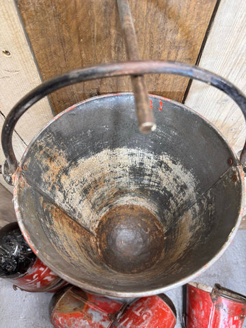 Vintage galvanised hanging fire bucket with rusty faded red paint and black handle used as a planter pail