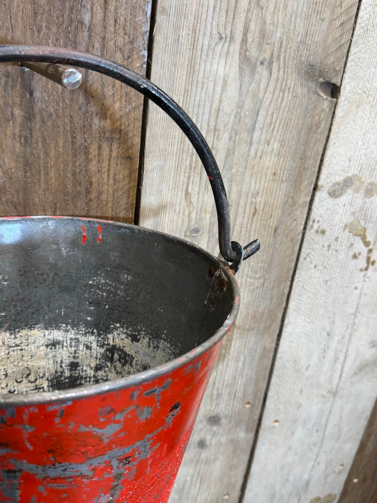Vintage galvanised hanging fire bucket in weathered red metal with black wrought iron handle and chipped paint